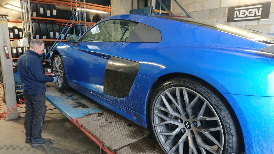 Technician at the wheel of a blue Audi R8 on the alignment ramp in the workshop