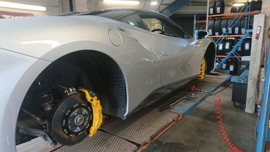 Silver Ferrari on the ramp with a front wheel off, showing its yellow brake caliper