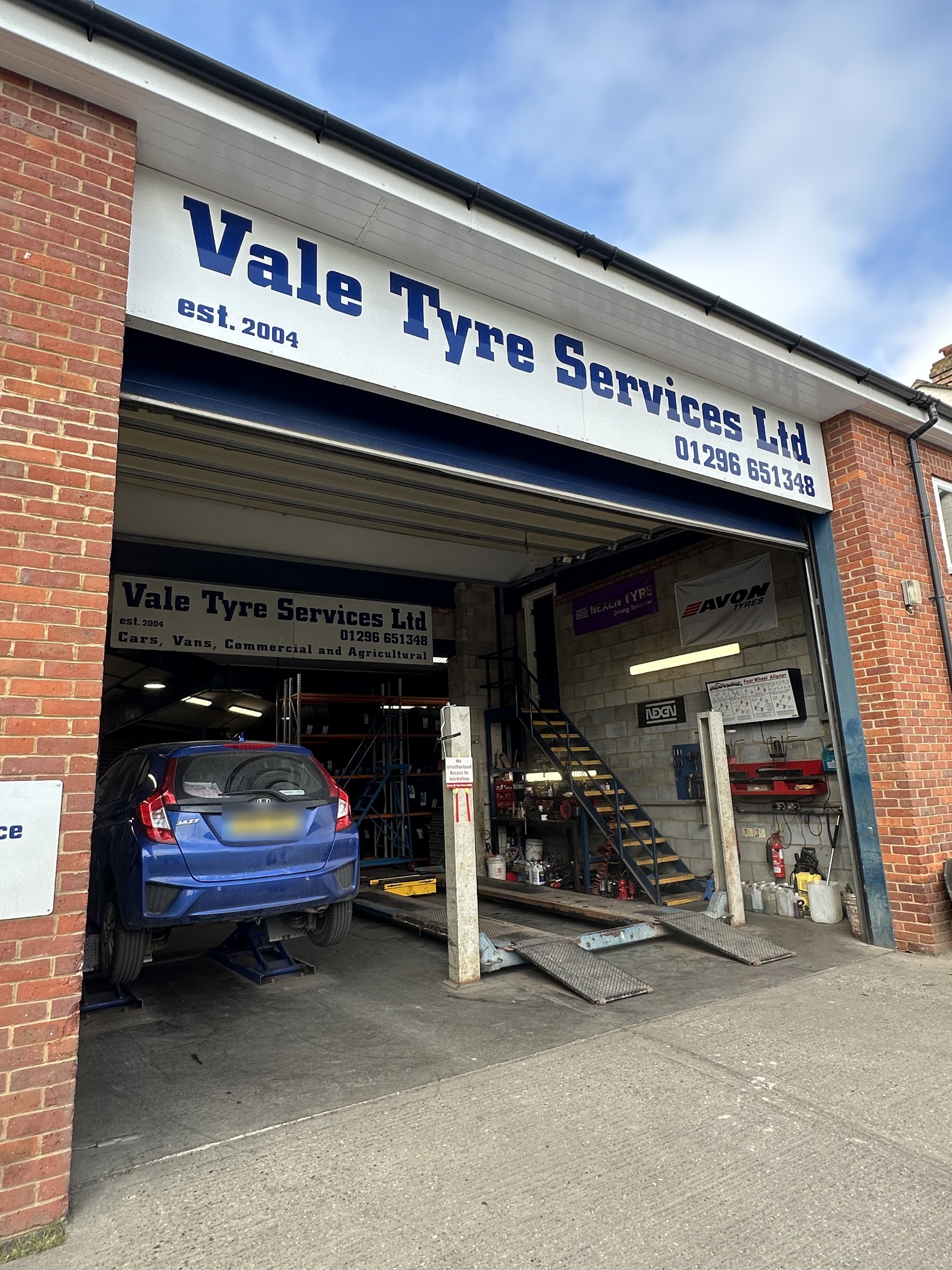 The open workshop bay with a car on the ramp and the inside sign for cars, vans, commercial and agricultural