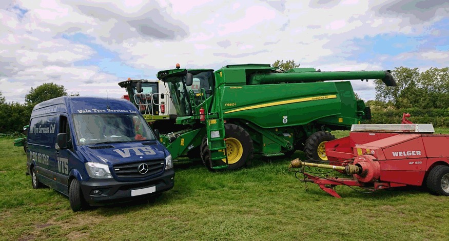 A Vale Tyre Services van in a field beside a green combine harvester and a red baler