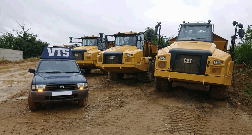 The VTS 4x4 on a muddy site in front of three yellow CAT dump trucks